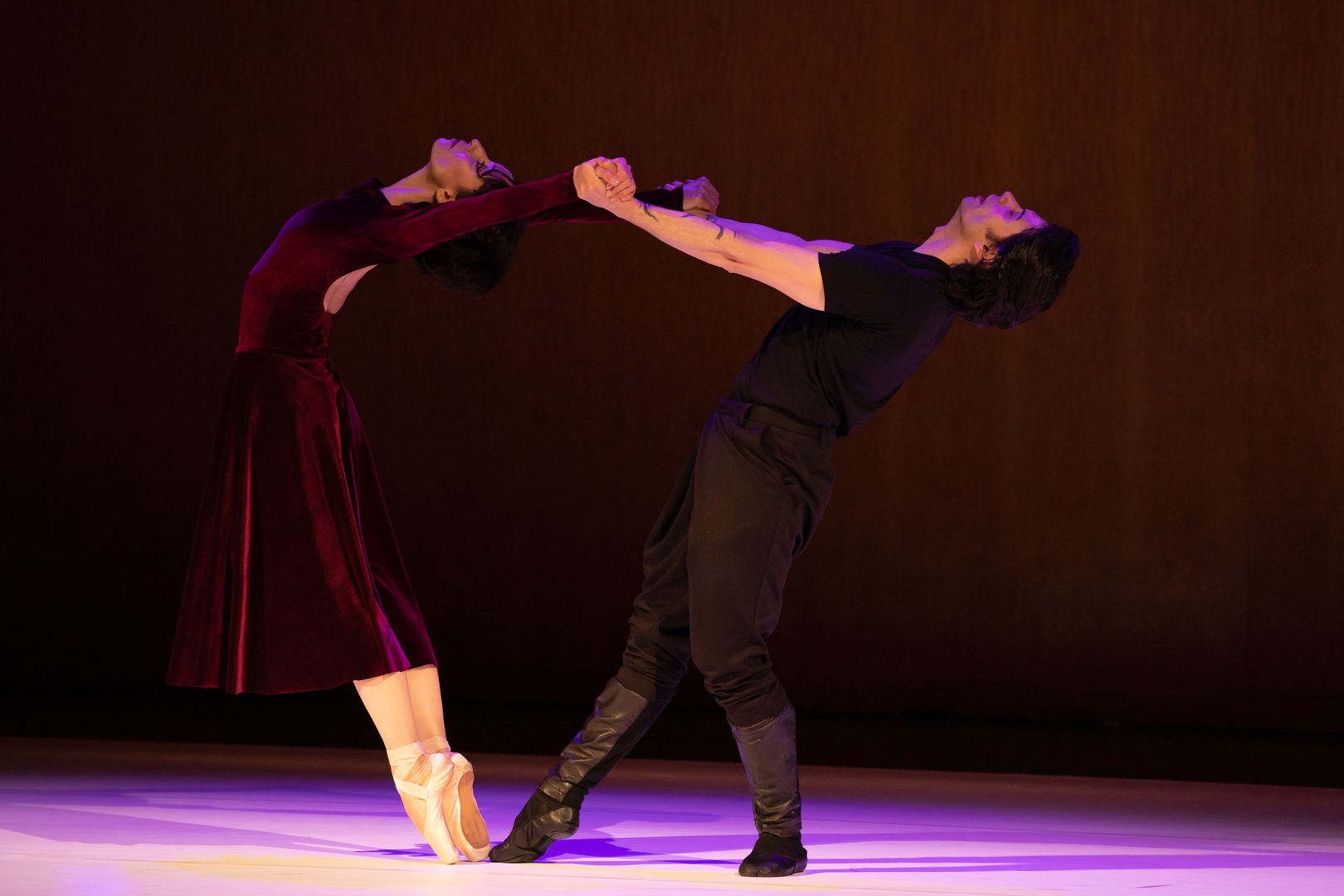 A woman (left) and a man strike a dance pose in purple light.